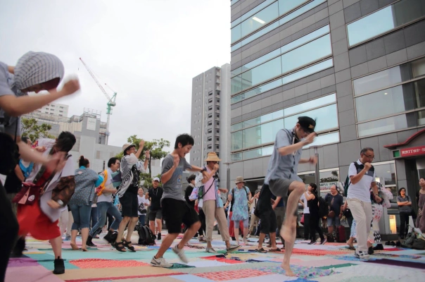 Dancing on top of patchwork O-Furoshiki at the 9th Sumida Street Jazz Festival in Tokyo, August 2018. The O-Furoshiki project started in 2011, where furushiki (meaning patches of cloth traditionally used to wrap/transport goods) are sewn together, symbolizing civic participation and the connecting of awareness that had been divided due to the nuclear incident. (Credit: Project FUKUSHIMA! / Sumida Street Jazz Festival)