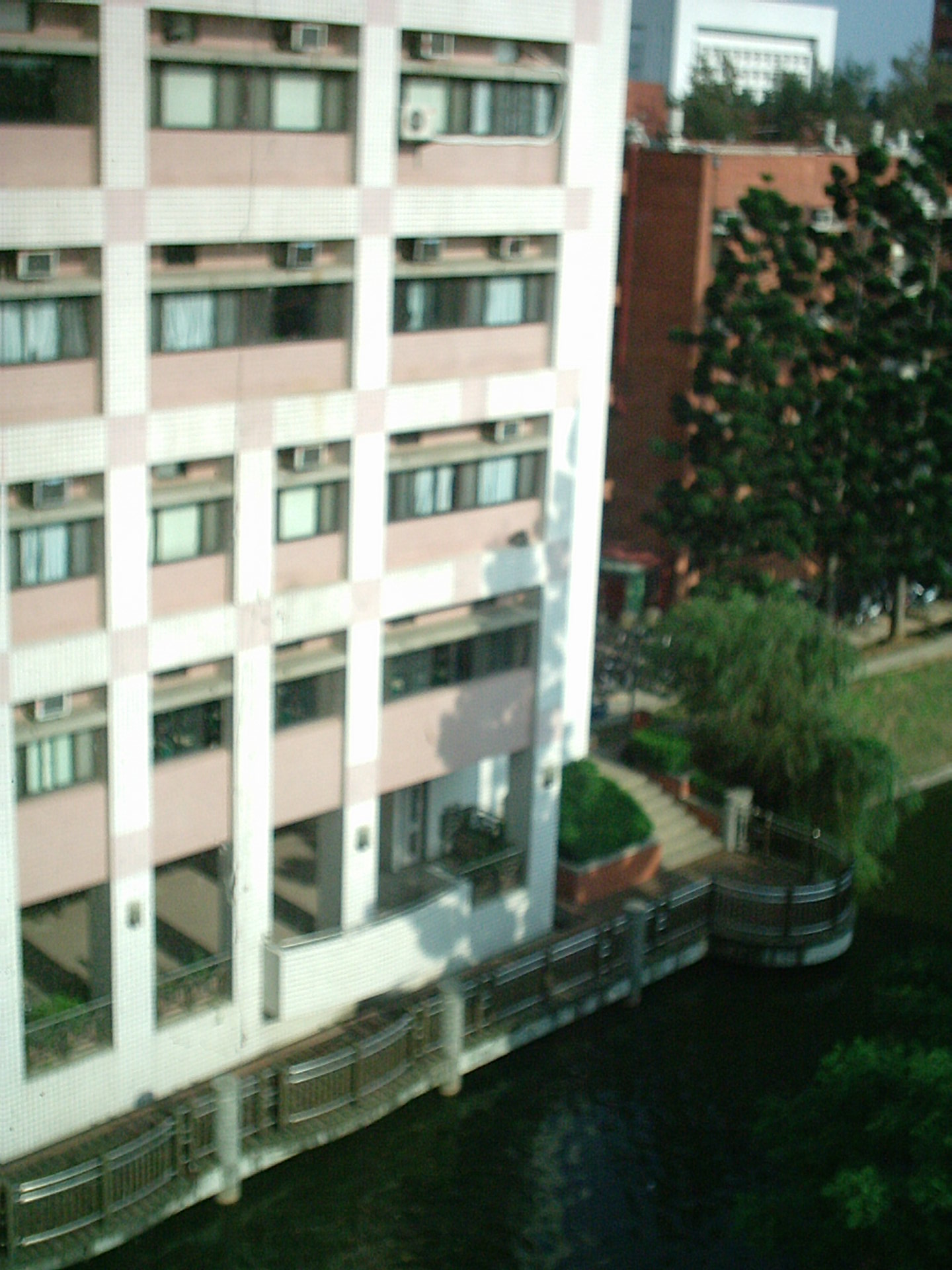 中央大學科四館是一個大L型建築物，這是在粘老師實驗室窗戶邊朝建築物另一側所拍的照片，很抱歉這是一張失焦的照片，但最起碼能分辨出建築物與湖畔步道。這些都是以前中央大學物理系學生經常出沒的地方。照片最上方五樓邊間，就是易臺生老師的實驗室，我大一大二經常在他實驗室廝混，學了很多實驗物理的技術。