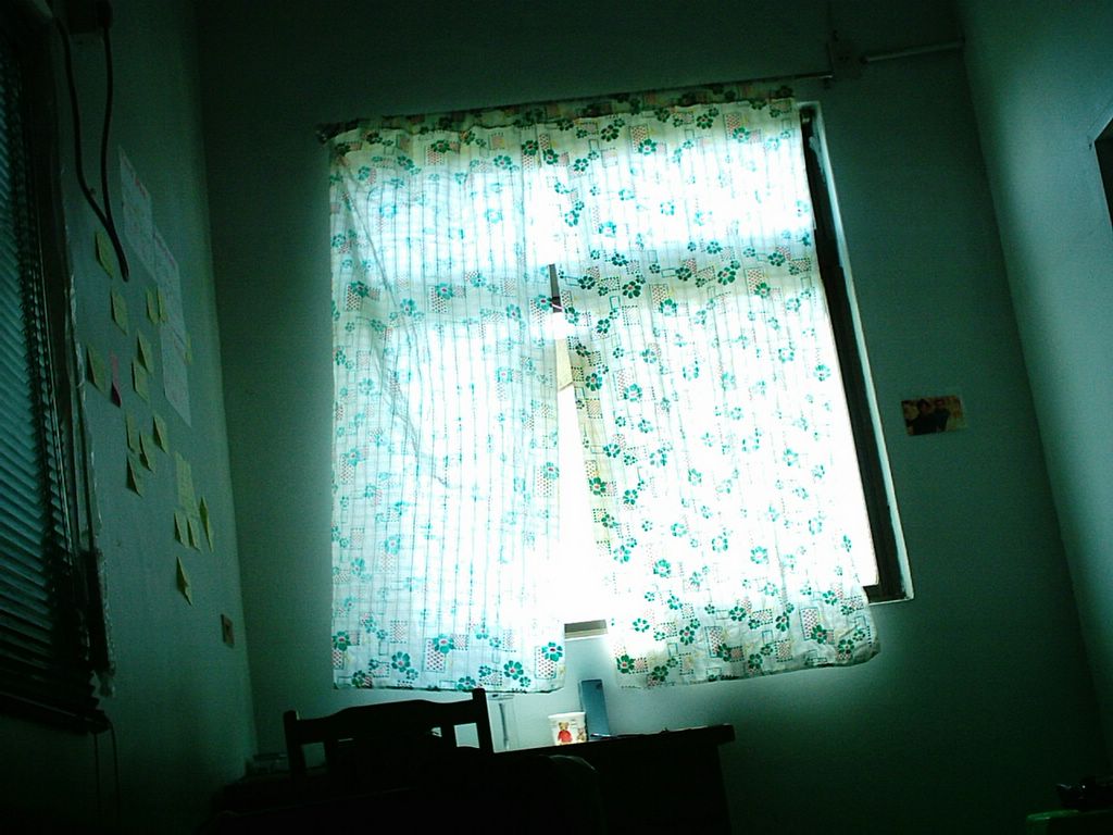住進來時房東所附的窗簾，這是我一生中用過最簡單的窗簾了，因為它就真的是只是薄透光的長條布，兩片布比窗戶再略長一些。想要讓陽光徹底灑進房間，人就必須站到書桌上將這兩條長條布捲收到上方的橫桿上，所以有時一天要好幾回站上書桌，一會將窗簾收上去，一會又嫌太熱太曬將窗簾再放下來。這張照片是我躺在床上，對著窗戶拍攝的相片。窗戶右邊的老舊插座，幾乎是吹風機專用的，所以每天晚上我會站在這插座前吹頭髮。